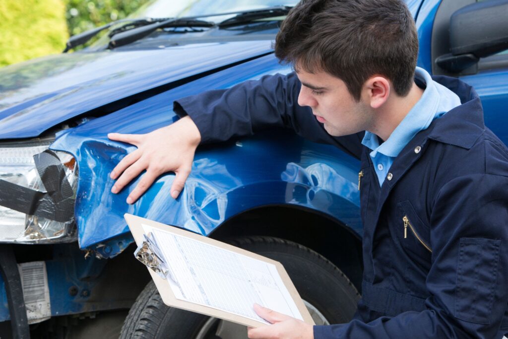 Mechanic inspecting blue car body damage with clipboard before repair estimate